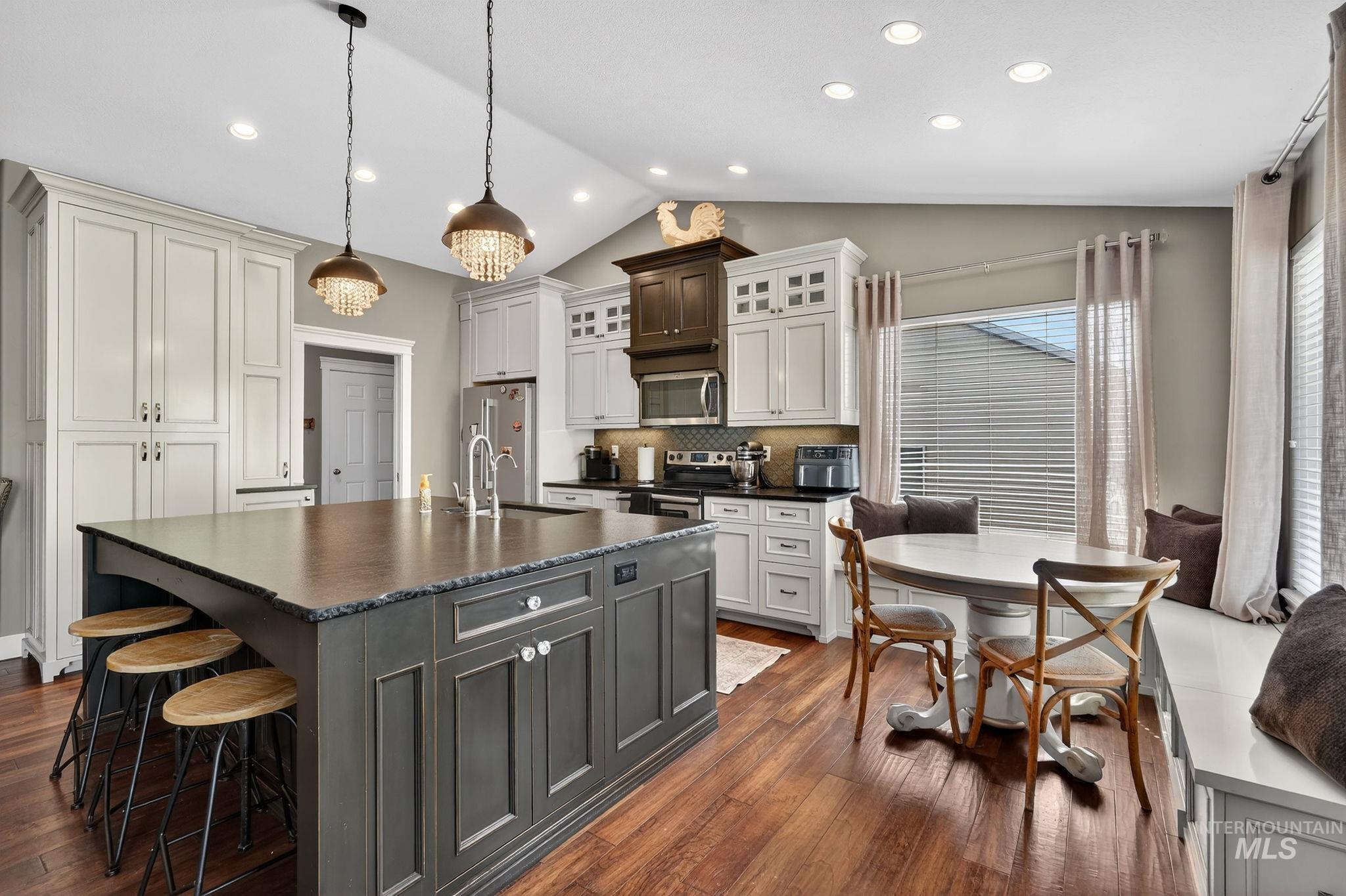 880 Redman Street Chubbuck, ID 83202 - Photo 8 of 39 Dual tone kitchen featuring two tone cabinetry, lofted ceiling, a center island with sink, glass fronted cabinets, and a kitchen bar