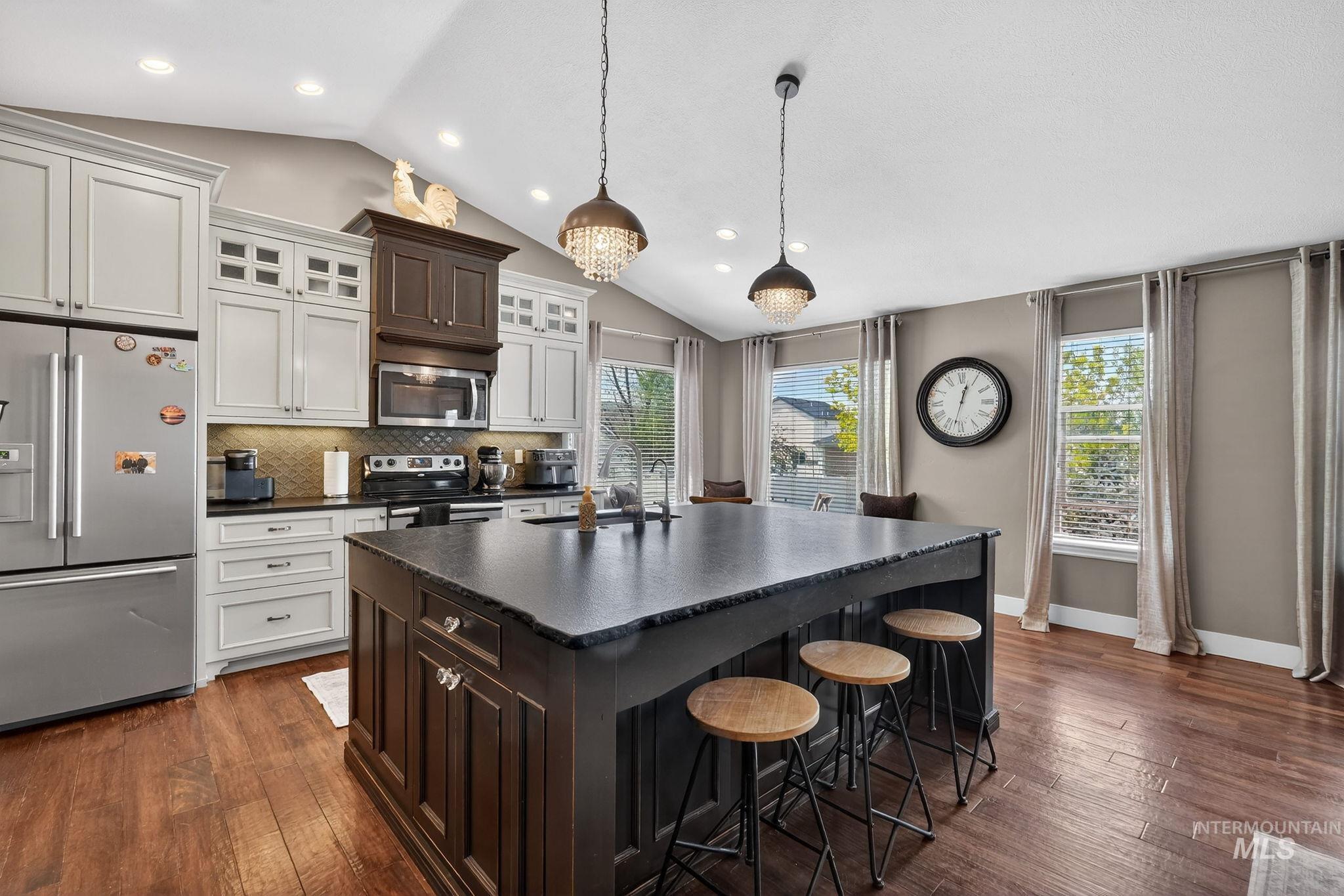 880 Redman Street Chubbuck, ID 83202 - Photo 9 of 39 Two tone kitchen with stainless steel appliances, dark wood finished floors, a kitchen bar, lofted ceiling, and glass insert cabinets