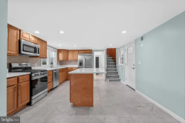 a large kitchen with stainless steel appliances granite countertop a stove top oven a sink and a refrigerator