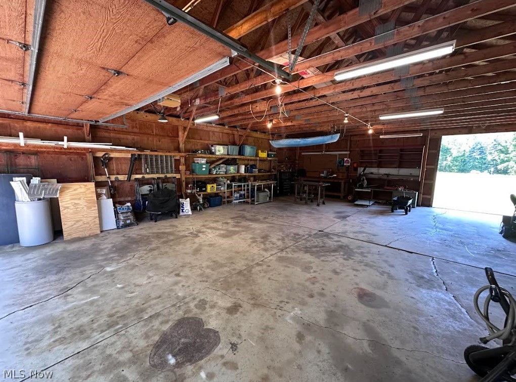 11292 Butternut Road Chardon, OH 44024 - Photo 46 of 49 Spacious garage featuring exposed wood beam ceiling, concrete flooring, overhead fluorescent lighting, built-in shelving, and an open garage door providing natural light