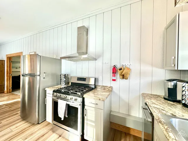 a kitchen with stainless steel appliances granite countertop a refrigerator a stove and a sink with wooden floor