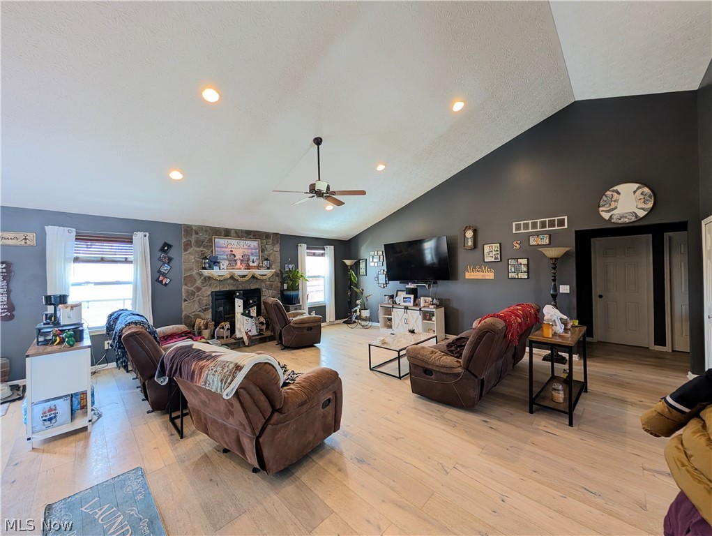 7360 Jones Road Nashport, OH 43830 - Photo 12 of 29 Living room with light wood-style flooring, a stone fireplace, a ceiling fan, recessed lighting, and a high textured ceiling