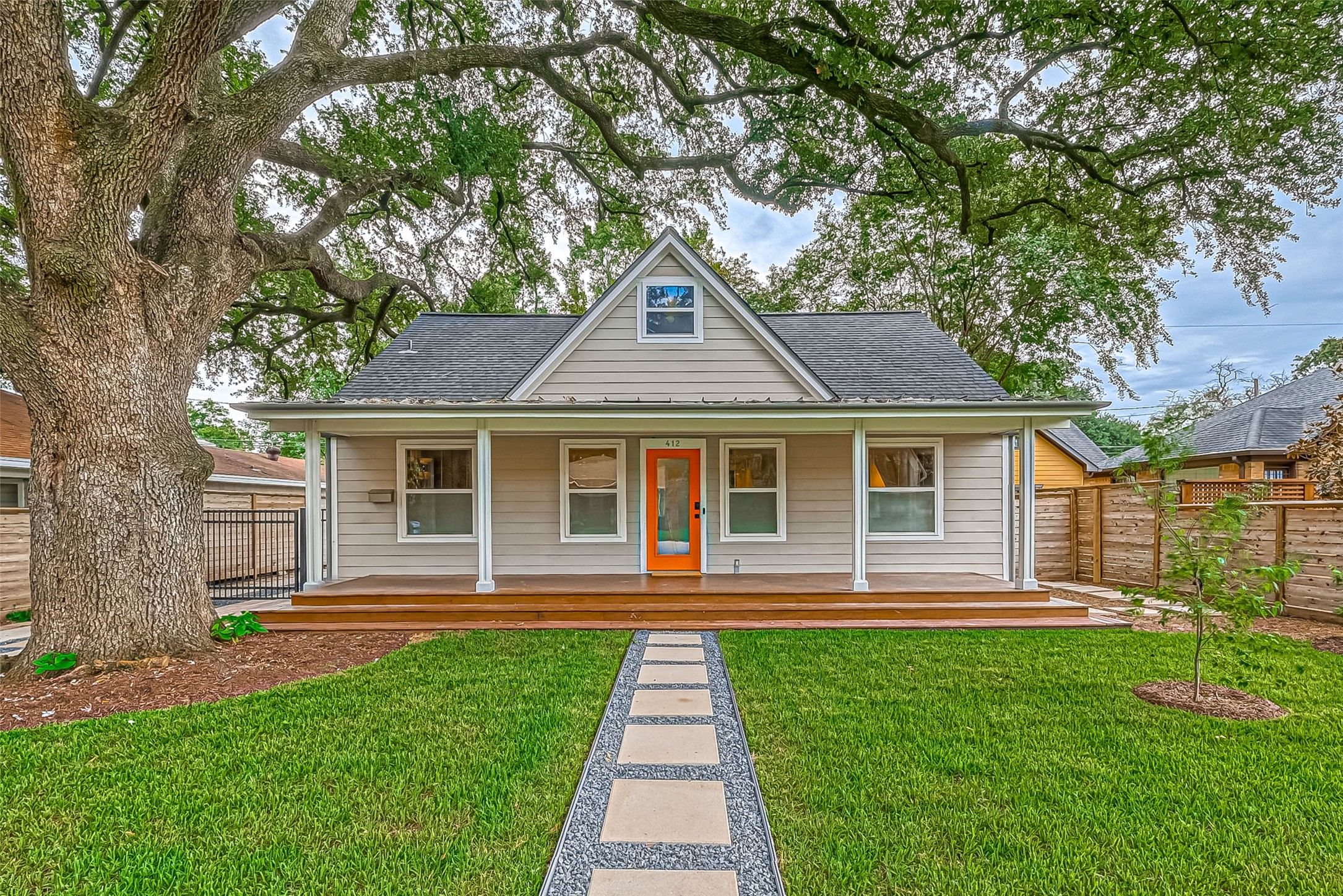 Charming home with inviting front porch and vibrant front door. It features a well-maintained lawn, a large shade tree, and a modern walkway leading to the entrance. The exterior has a classic, cozy appeal.