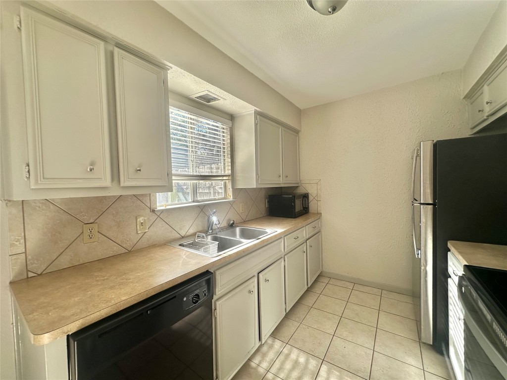 11907 Argonne Forest Trail, Unit B Austin, TX 78759 - Photo 3 of 11 Kitchen with black appliances, a textured wall, light countertops, light tile patterned floors, and backsplash