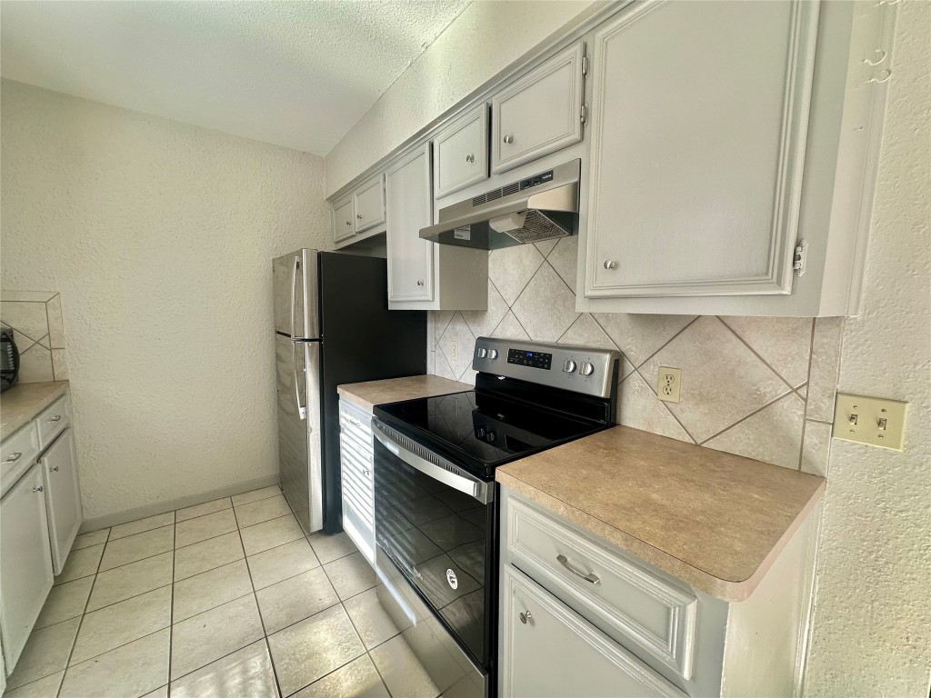 11907 Argonne Forest Trail, Unit B Austin, TX 78759 - Photo 4 of 11 Kitchen with a textured wall, electric range, under cabinet range hood, light countertops, and light tile patterned floors