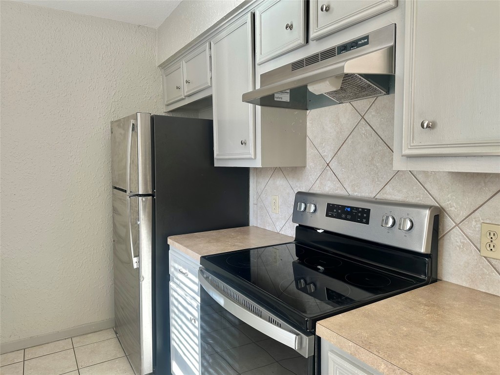 11907 Argonne Forest Trail, Unit B Austin, TX 78759 - Photo 5 of 11 Kitchen featuring a textured wall, electric range, light countertops, under cabinet range hood, and light tile patterned floors