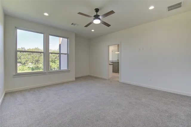 an empty room with chandelier fan and windows