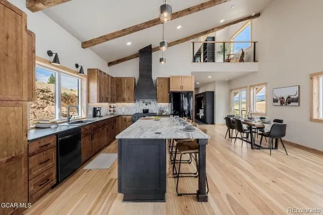 a kitchen with stainless steel appliances granite countertop a kitchen island a stove a refrigerator a sink dishwasher a dining table and chairs with wooden floor