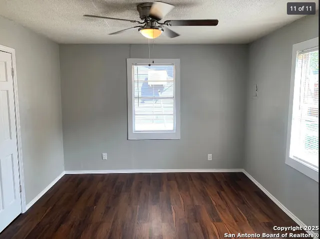 an empty room with wooden floor chandelier fan and windows