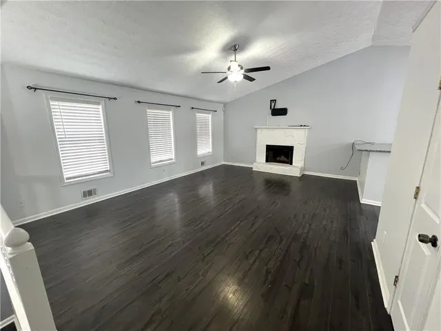 an empty room with wooden floor fireplace and windows
