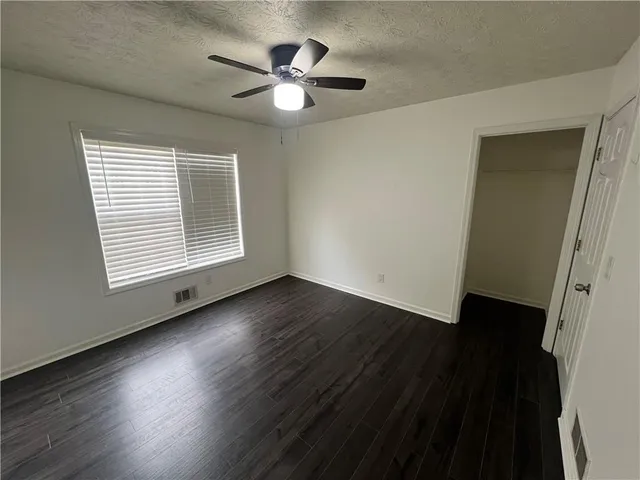 an empty room with wooden floor chandelier fan and windows