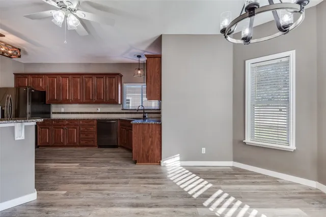 a large kitchen with granite countertop a stove top oven a sink dishwasher and wooden cabinets