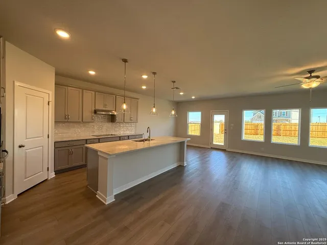 a view of an empty room with wooden floor and a ceiling fan