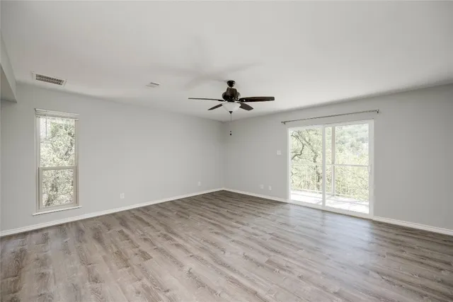 an empty room with wooden floor chandelier fan and windows