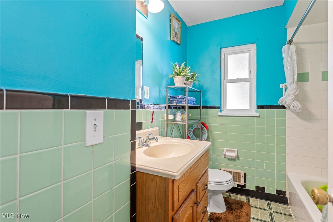 Full bath featuring vanity, tile walls, tile patterned floors, and a wainscoted wall