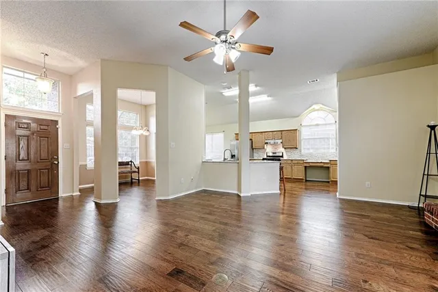 a view of an empty room and kitchen with wooden floor