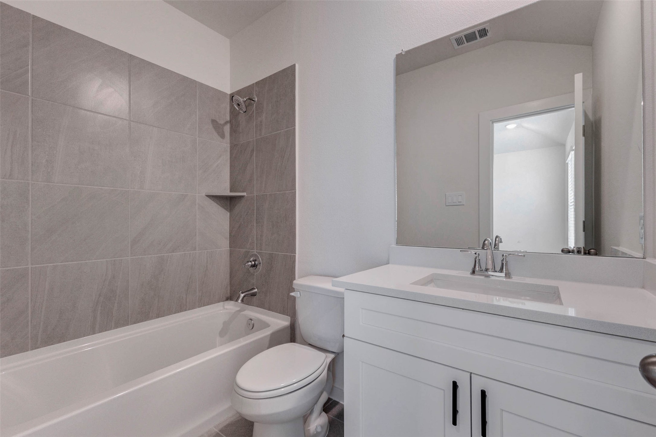 1206 Hemet Court Rosharon, TX 77583 - Photo 19 of 21 Full secondary bath featuring a white vanity, quartz-style countertop, large mirror, tub/shower combination, gray tile surround, and black cabinet hardware. The clean neutral palette feels fresh and modern, while the practical layout offers everything needed for guests or secondary bedrooms in a bright, low-maintenance space.