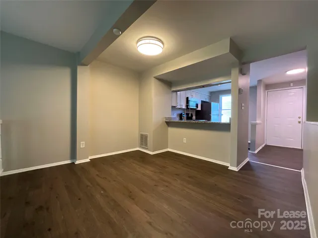 an empty room with wooden floor and a kitchen