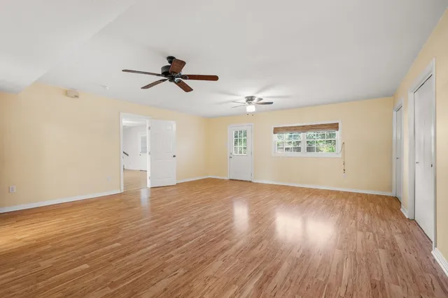 an empty room with wooden floor ceiling fan and windows