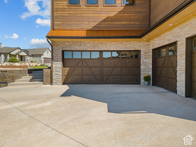 1192 East Ashdown Road Cedar City, UT 84721 - Photo 9 of 96 Wood-finish garage doors with window panels, stone veneer exterior, wood siding, concrete driveway, and stone retaining wall with steps