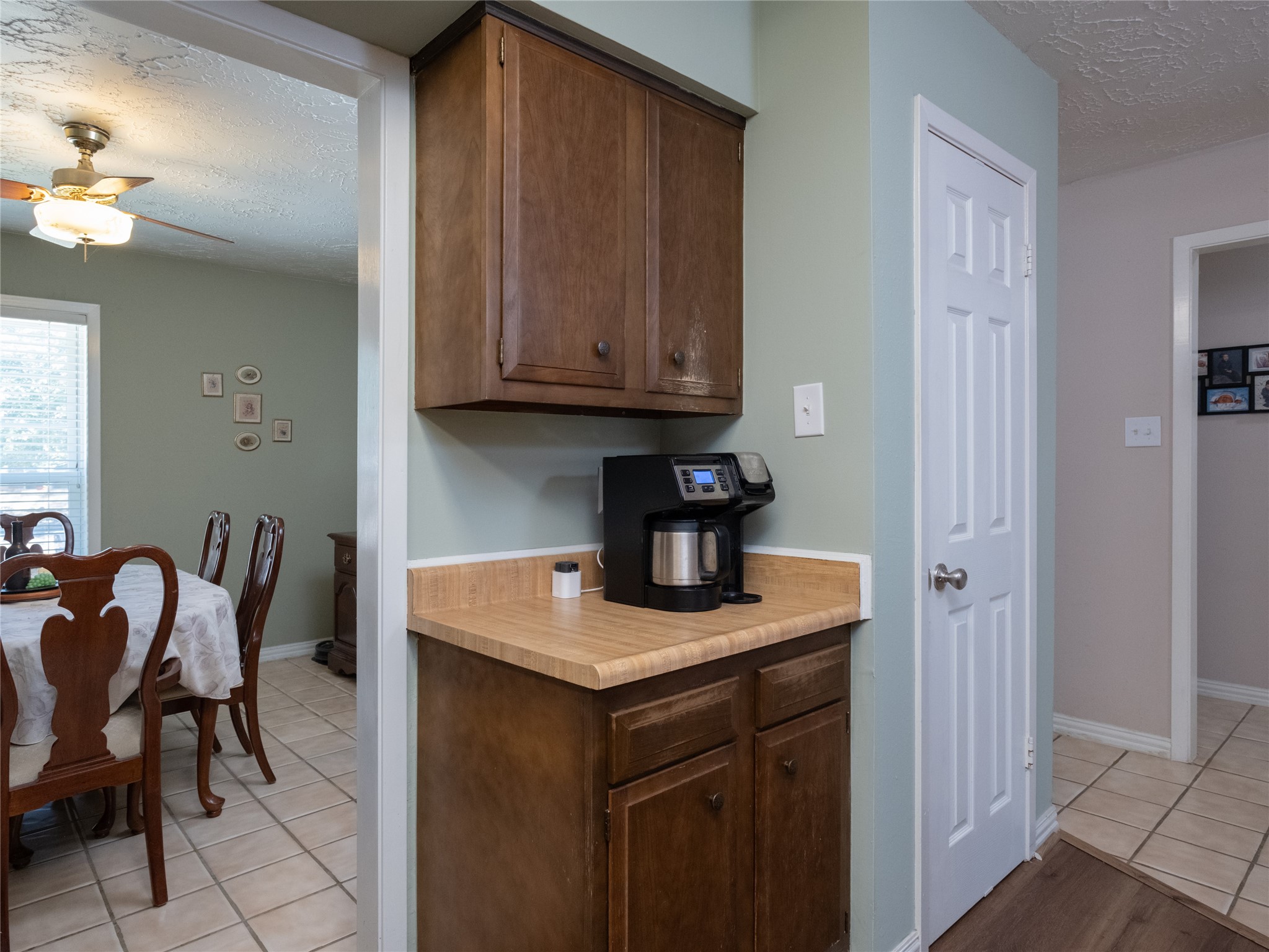 7315 Weatherhill Lane Houston, TX 77041 - Photo 12 of 40 This photo shows a cozy kitchen nook to create a coffee serving area. Adjacent is a dining area with a ceiling fan and natural light from a window, creating a warm, inviting atmosphere.