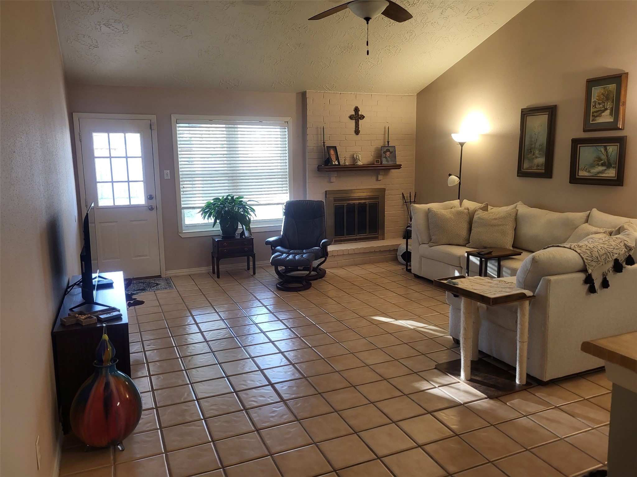 7315 Weatherhill Lane Houston, TX 77041 - Photo 15 of 40 This cozy family room features a tiled floor, a white brick fireplace, and a vaulted ceiling. Natural light streams in through a window, enhancing the warm, inviting atmosphere.