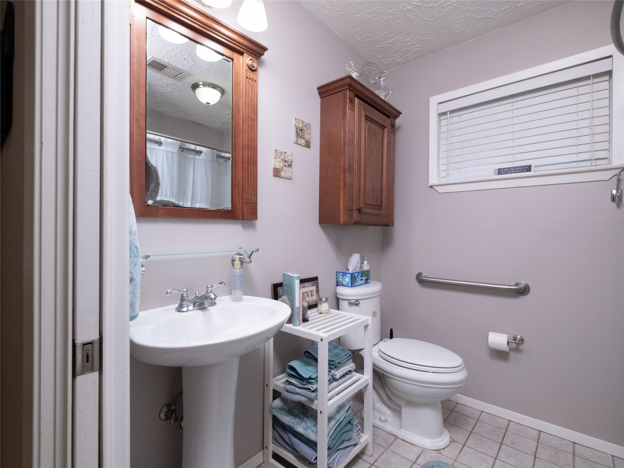 7315 Weatherhill Lane Houston, TX 77041 - Photo 19 of 40 This bathroom features a pedestal sink with a large mirror with storage and overhead lighting. It also includes a wooden cabinet for storage. The space is well-lit and has a neutral color palette.