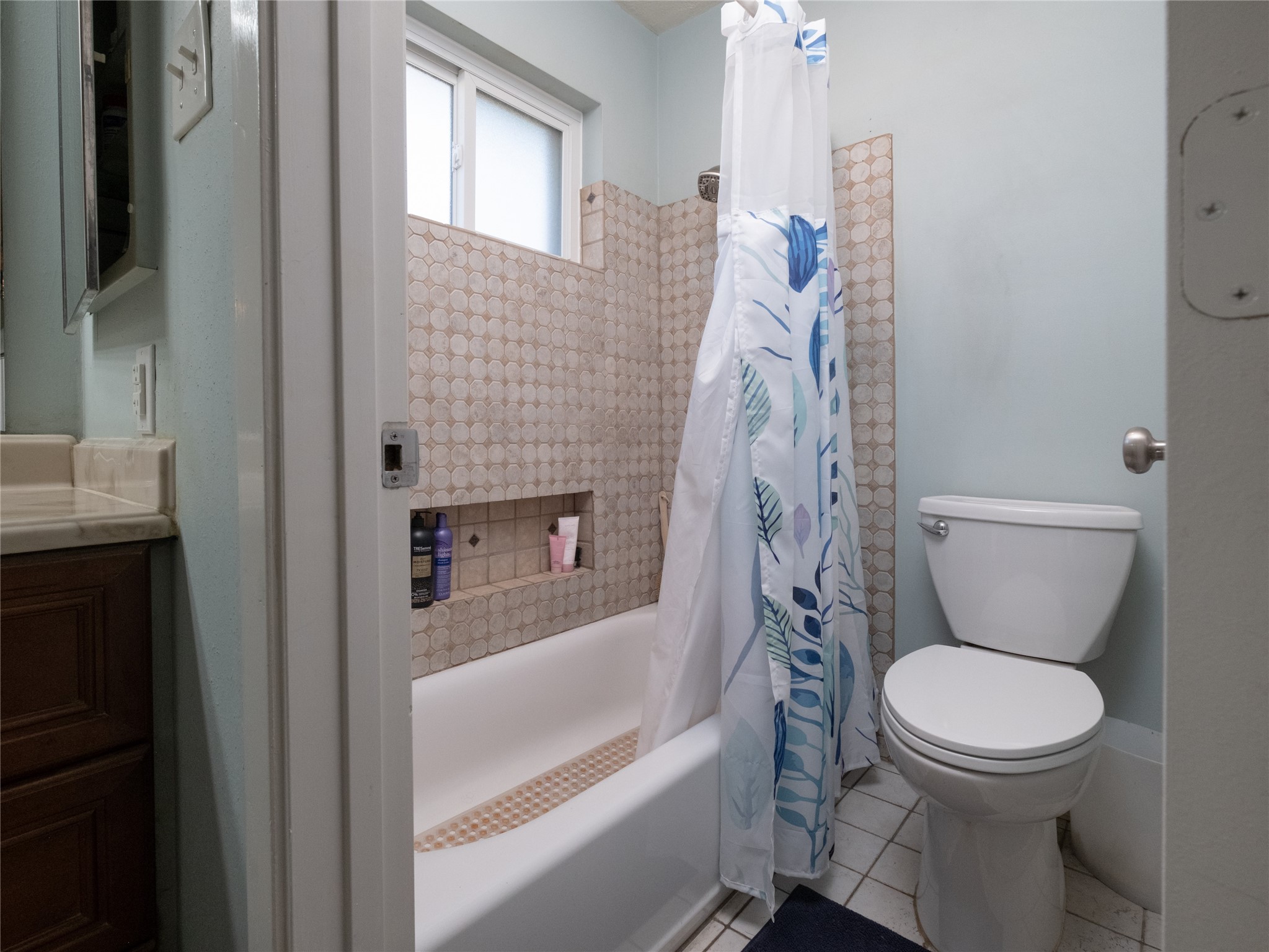7315 Weatherhill Lane Houston, TX 77041 - Photo 29 of 40 This bathroom features a classic design with a bathtub and shower, complemented by a patterned tile surround. The space is well-lit by a frosted window, providing privacy while allowing natural light.