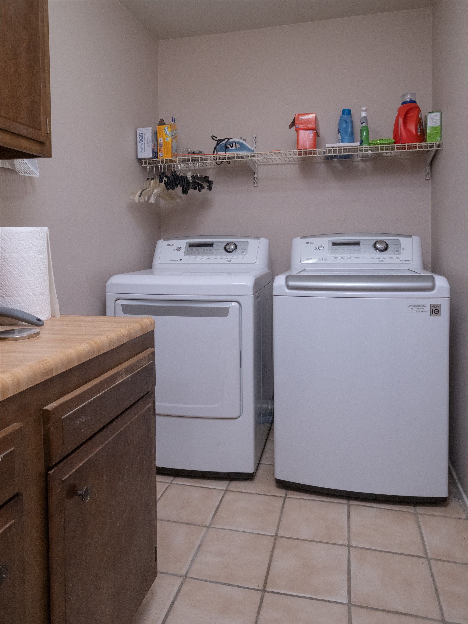 7315 Weatherhill Lane Houston, TX 77041 - Photo 31 of 40 This laundry room features tiled flooring, a wooden cabinet for storage, and a wire shelf above the appliances for additional storage of cleaning supplies and hangers.