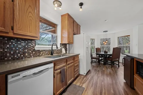 a kitchen with stainless steel appliances granite countertop a refrigerator a sink dishwasher a stove and white countertops with wooden floor