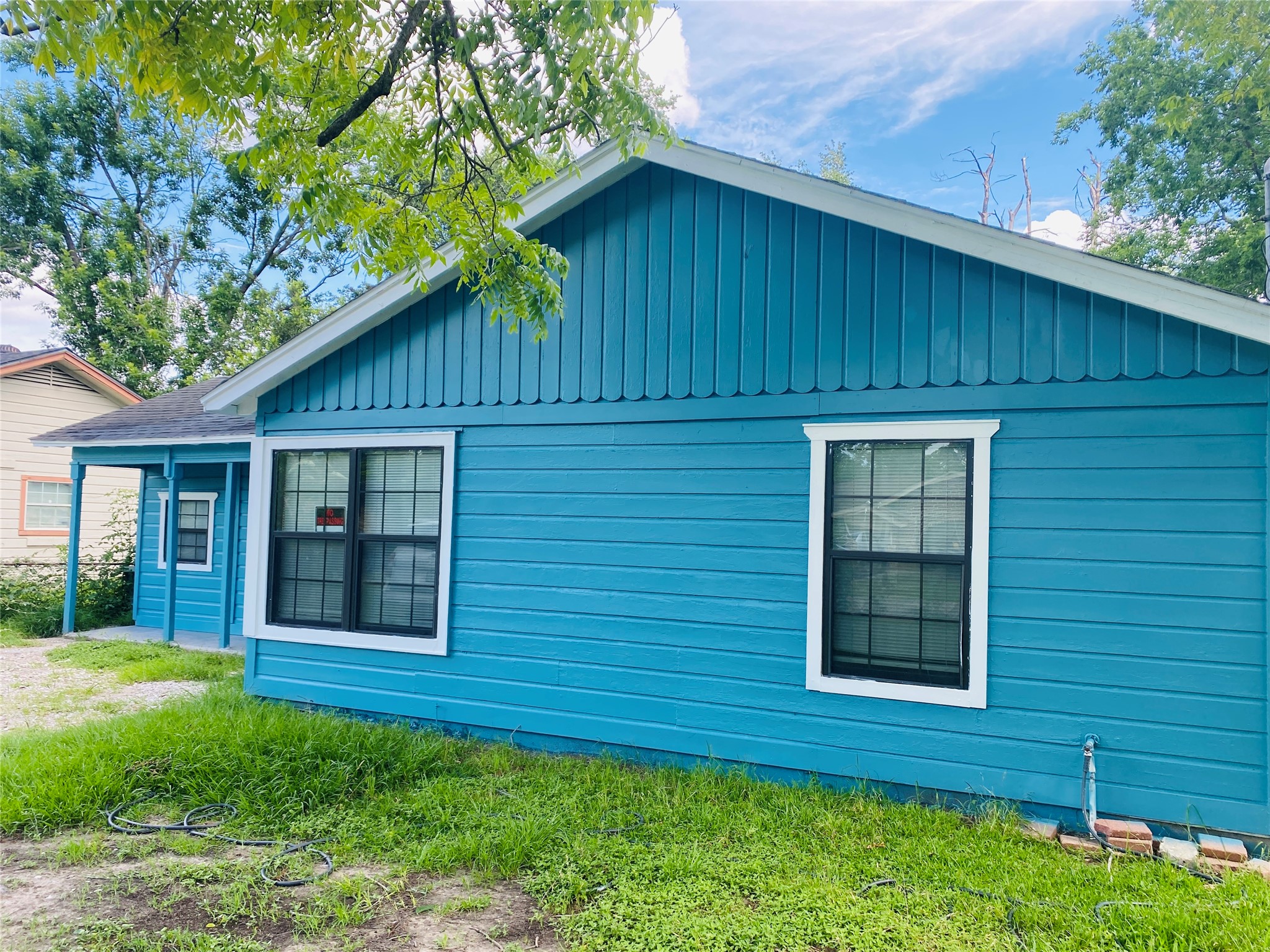 7547 Laura Koppe Road Houston, TX 77028 - Photo 2 of 11 Charming single-story home with a vibrant blue exterior and white trim. Features large windows for natural light and a cozy covered porch. Surrounded by lush greenery, perfect for a serene setting.