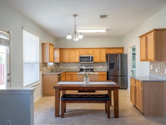 a kitchen with stainless steel appliances kitchen island granite countertop a sink dishwasher a stove a refrigerator a dining table and chairs with wooden floor
