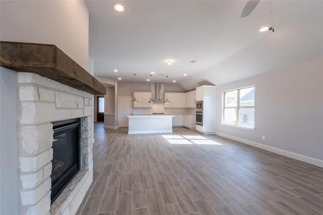 a view of an empty room with wooden floor and a kitchen