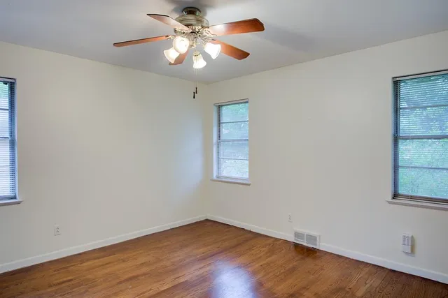 an empty room with wooden floor chandelier fan and windows