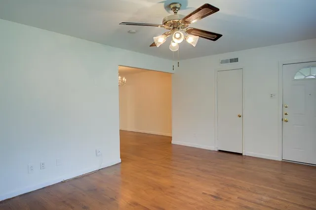 an empty room with wooden floor fan and windows