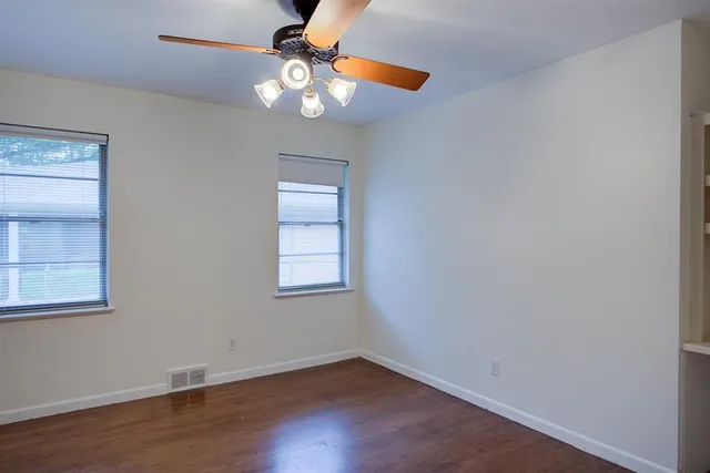 an empty room with wooden floor fan and windows