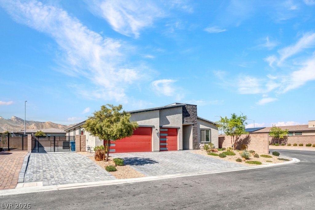 Contemporary home with a garage, stone siding, decorative driveway, stucco siding, and a gate