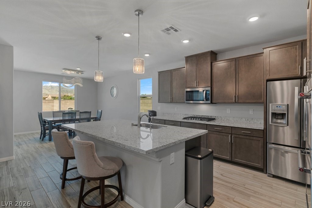 4191 Velvet View Street Las Vegas, NV 89129 - Photo 8 of 44 Kitchen with light stone counters, wood finish floors, a kitchen breakfast bar, stainless steel appliances, and an island with sink