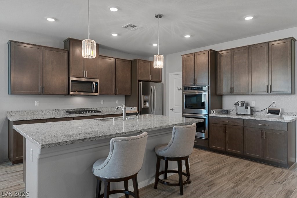 4191 Velvet View Street Las Vegas, NV 89129 - Photo 9 of 44 Kitchen with dark wood finish cabinets, light stone counters, light wood-style flooring, and stainless steel appliances
