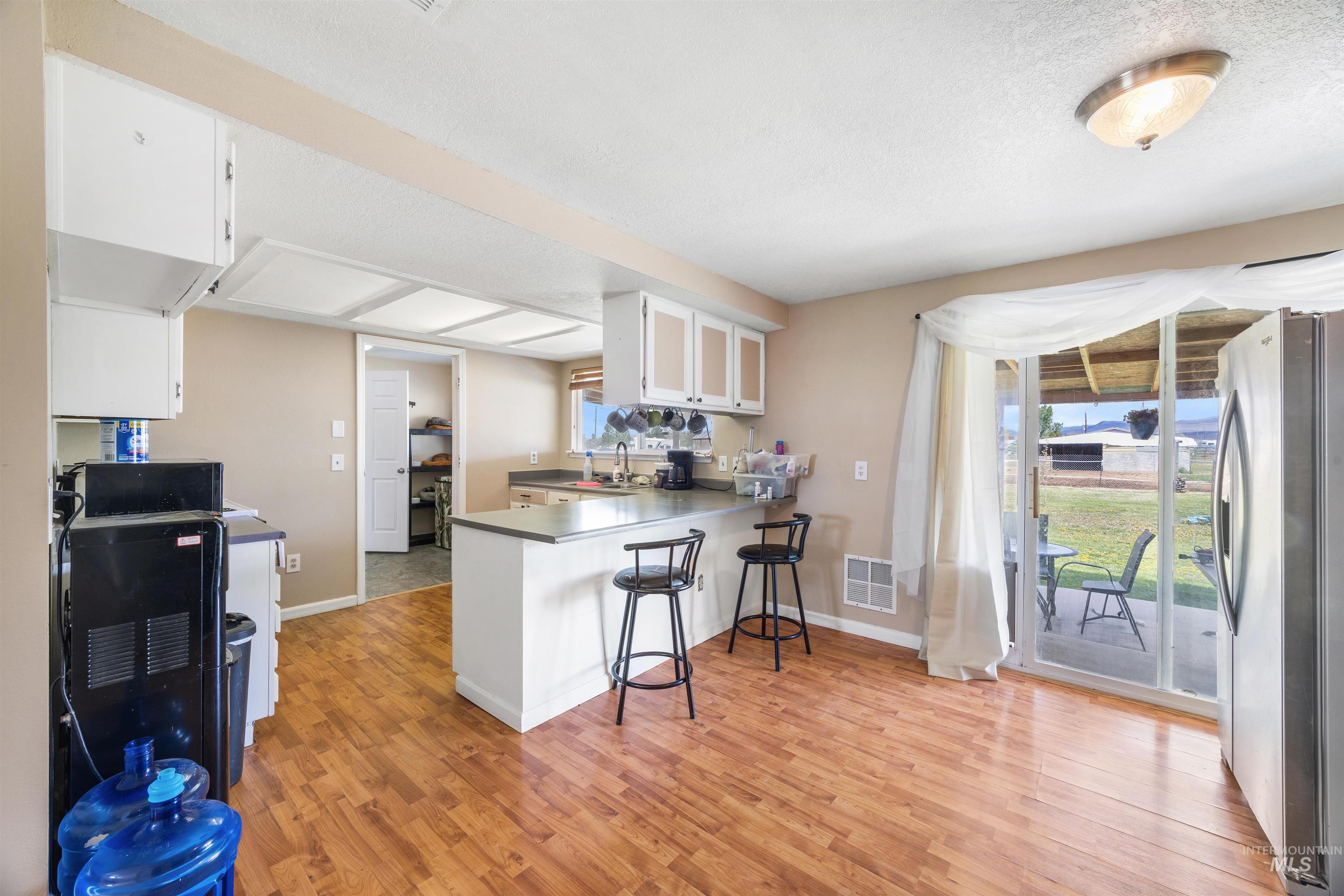 3044 Northeast Reservoir Road Mountain Home, ID 83647 - Photo 12 of 34 Kitchen featuring wood-finish flooring, white cabinetry, a kitchen island with seating, a stainless steel refrigerator, and sliding glass doors opening to an outdoor patio
