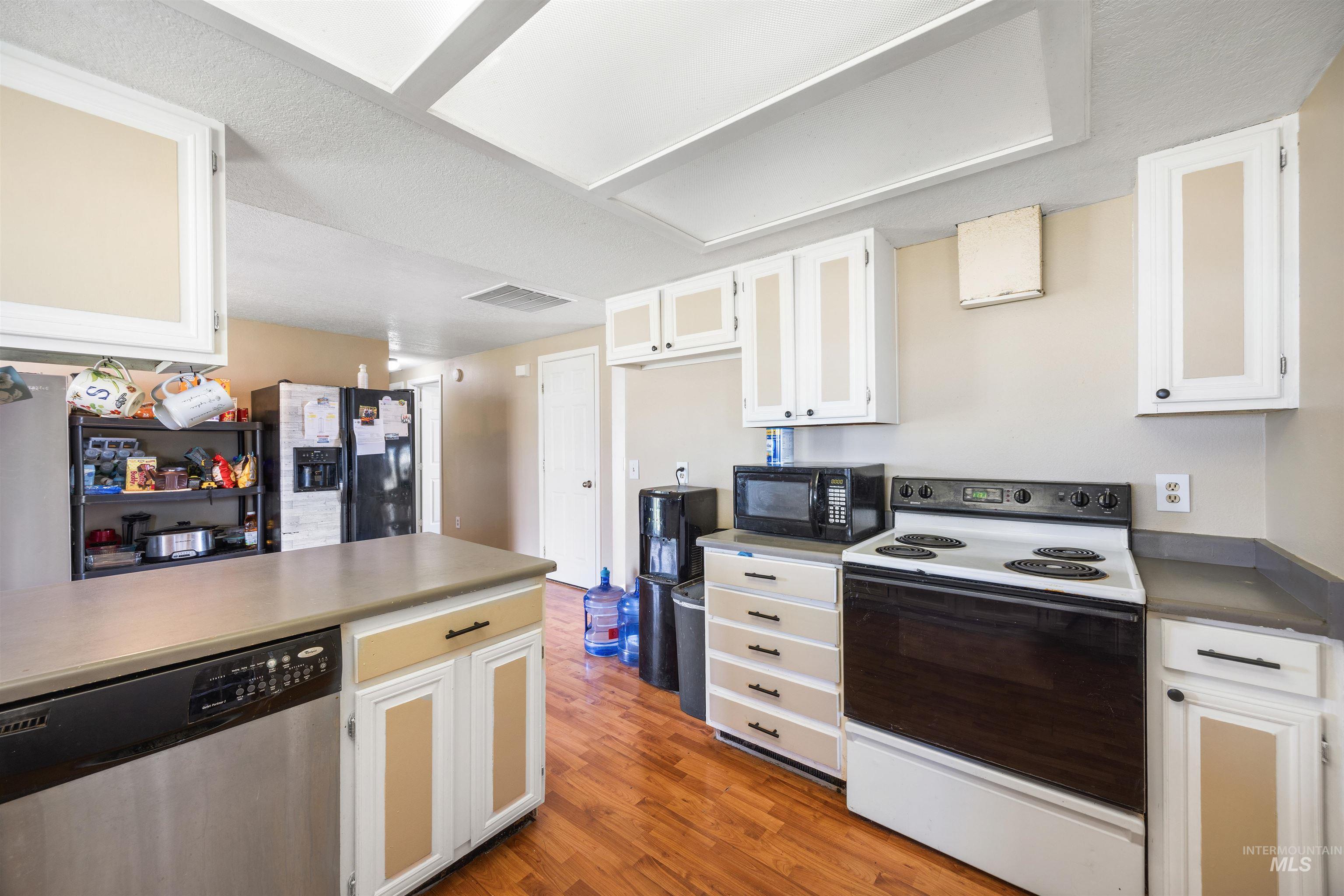 3044 Northeast Reservoir Road Mountain Home, ID 83647 - Photo 13 of 34 Kitchen featuring wood-finish flooring, white cabinetry with light-toned inserts, gray countertops, and a stainless steel dishwasher