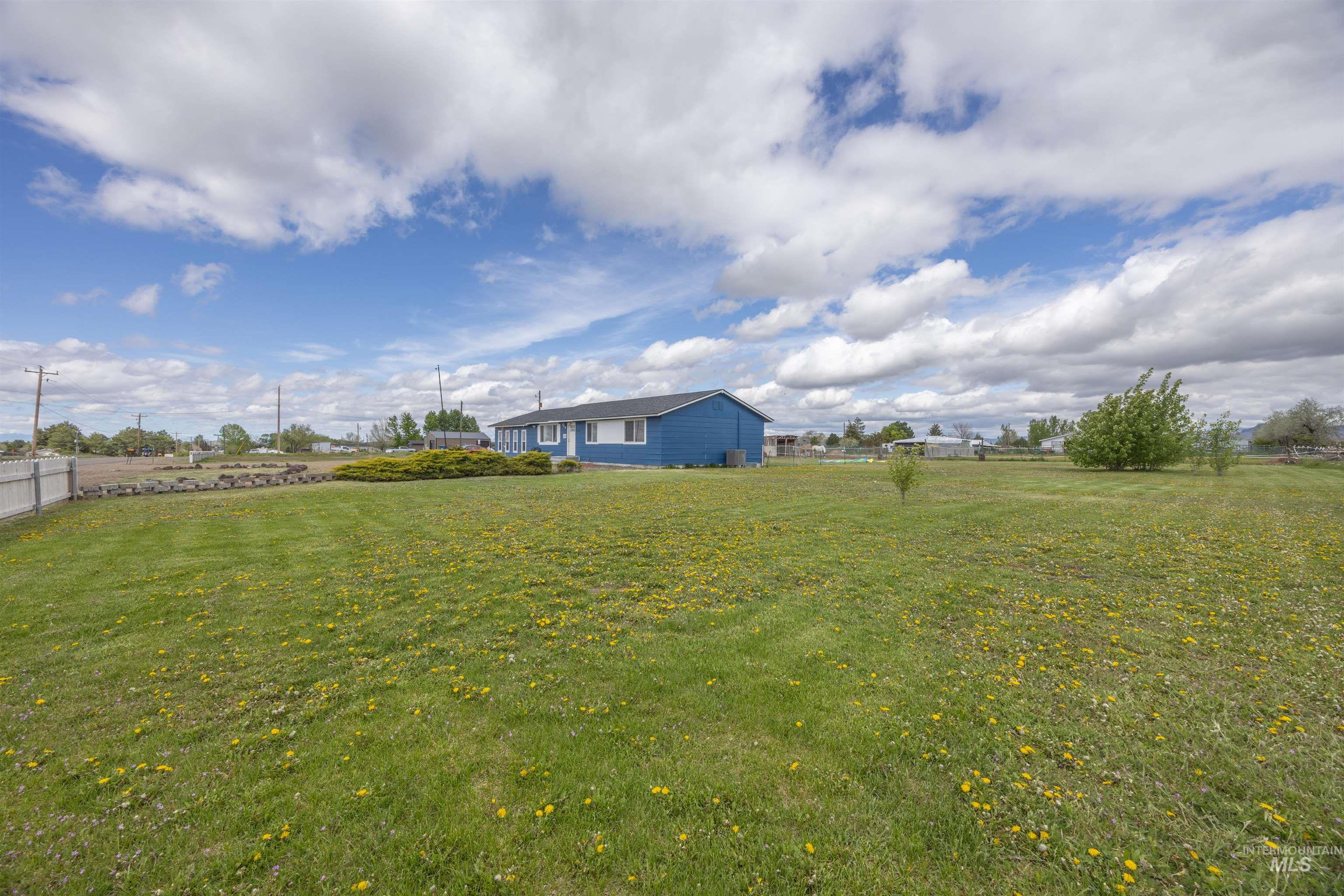 3044 Northeast Reservoir Road Mountain Home, ID 83647 - Photo 18 of 34 Expansive green lawn with a partial fence perimeter, featuring a single-story blue residence with white trim and a dark roof