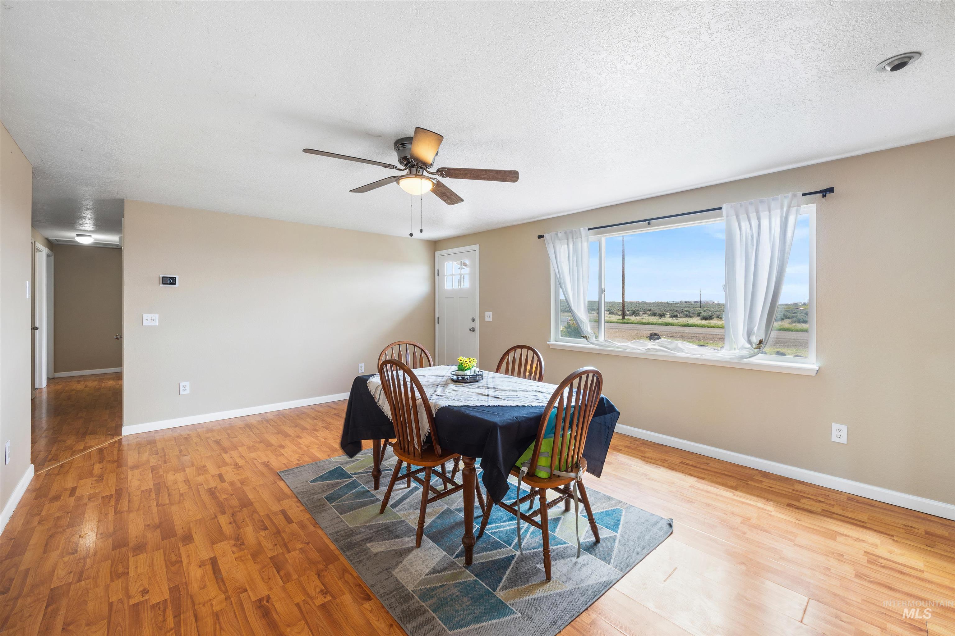 3044 Northeast Reservoir Road Mountain Home, ID 83647 - Photo 21 of 34 Open-concept room featuring wood-finish flooring, a ceiling fan with integrated lighting, a large window with a distant landscape, and a hallway entry