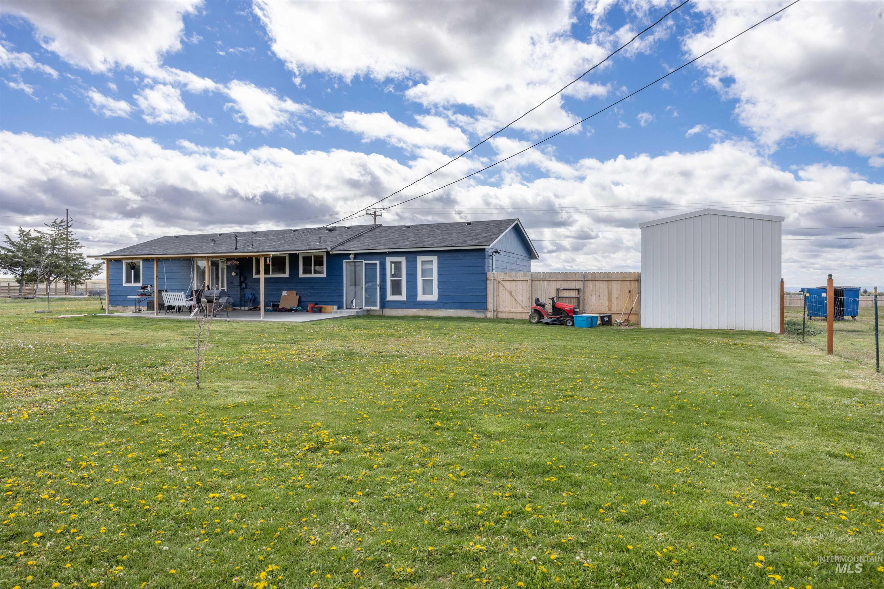 3044 Northeast Reservoir Road Mountain Home, ID 83647 - Photo 26 of 34 Expansive green yard with a blue-sided residence featuring multiple windows and a covered patio