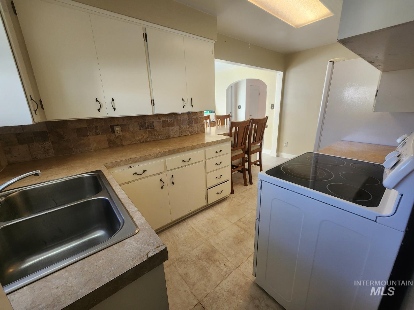 219 South 7th Street Nyssa, OR 97913 - Photo 3 of 29 Kitchen featuring white appliances, arched walkways, backsplash, white cabinets, and light countertops