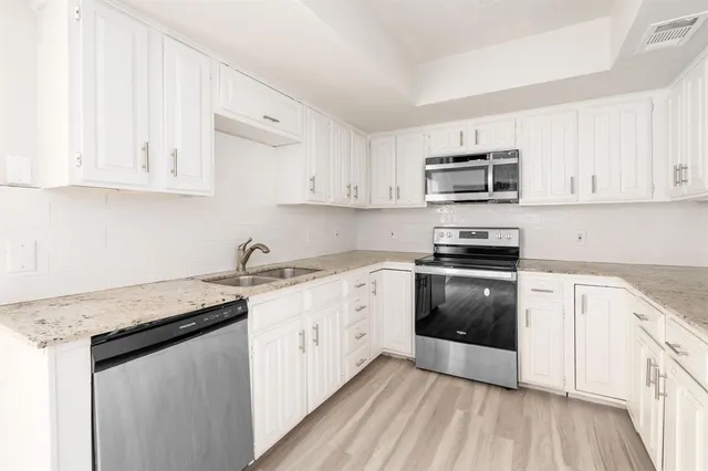 a kitchen with stainless steel appliances granite countertop a stove a sink and white cabinets