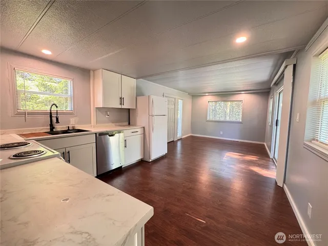 a open kitchen with white cabinets a sink dishwasher a stove and a refrigerator with wooden floor