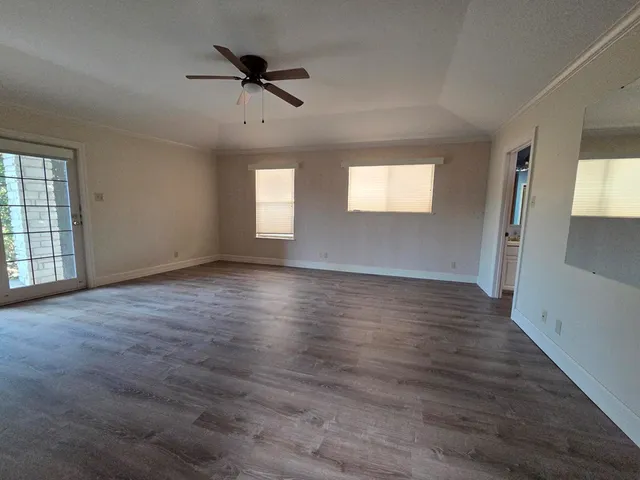 an empty room with wooden floor fan and windows