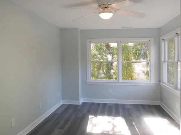 an empty room with wooden floor fan and windows