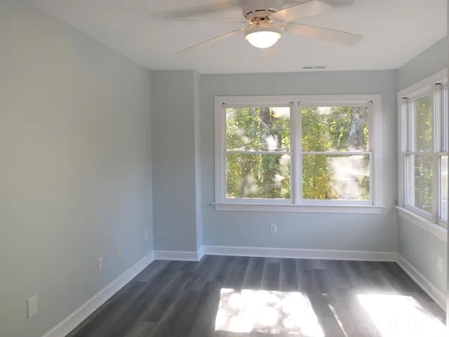 an empty room with wooden floor fan and windows